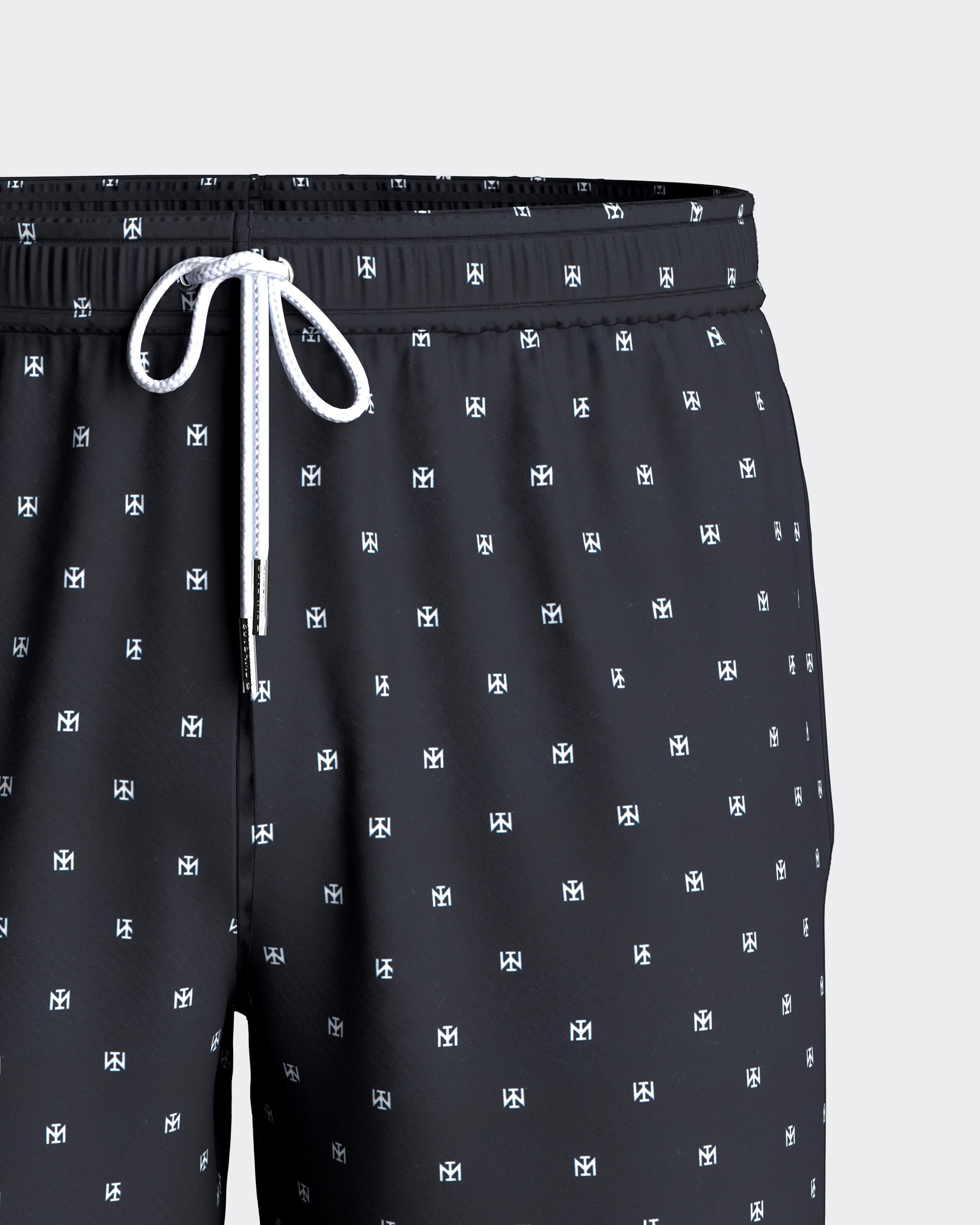 Maison Sarava men's black swim trunks with micro Impetus logo pattern, drawstring waist, side pockets, and inner mesh lining.