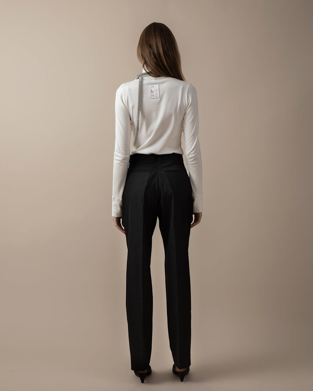 Maison Sarava black high-waist trousers with straight fit, two front patch pockets, and A-design stitching on back patch pockets. Cut detail below knee.