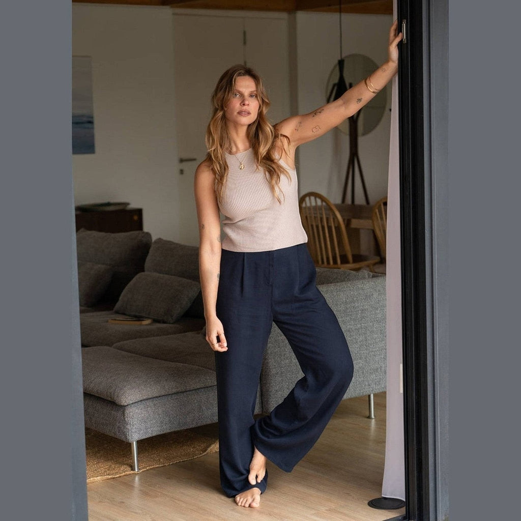 Maison Sarava navy wide leg pleated trousers on a woman standing indoors.