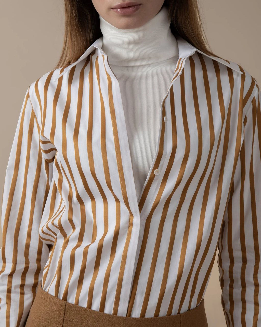 Maison Sarava women's white and gold striped fitted shirt with pointed collar, worn over a white turtleneck.