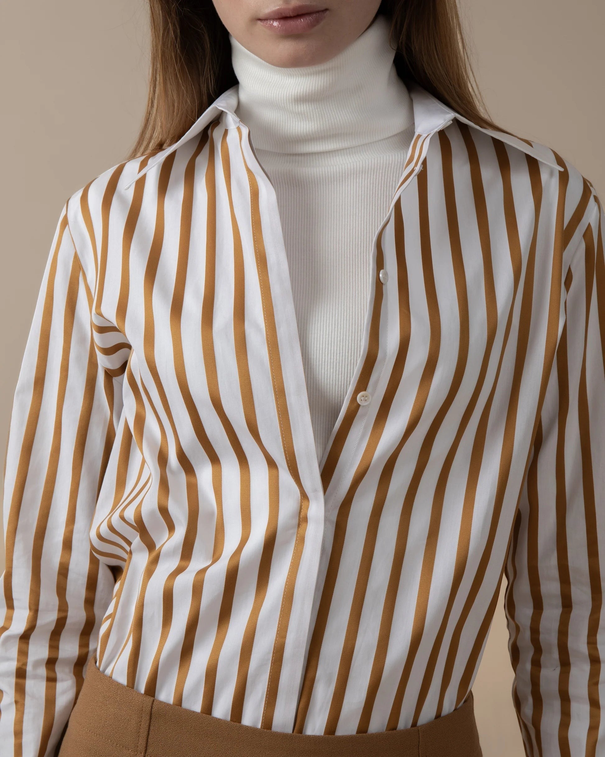 Maison Sarava women's white and gold striped fitted shirt with pointed collar, worn over a white turtleneck.