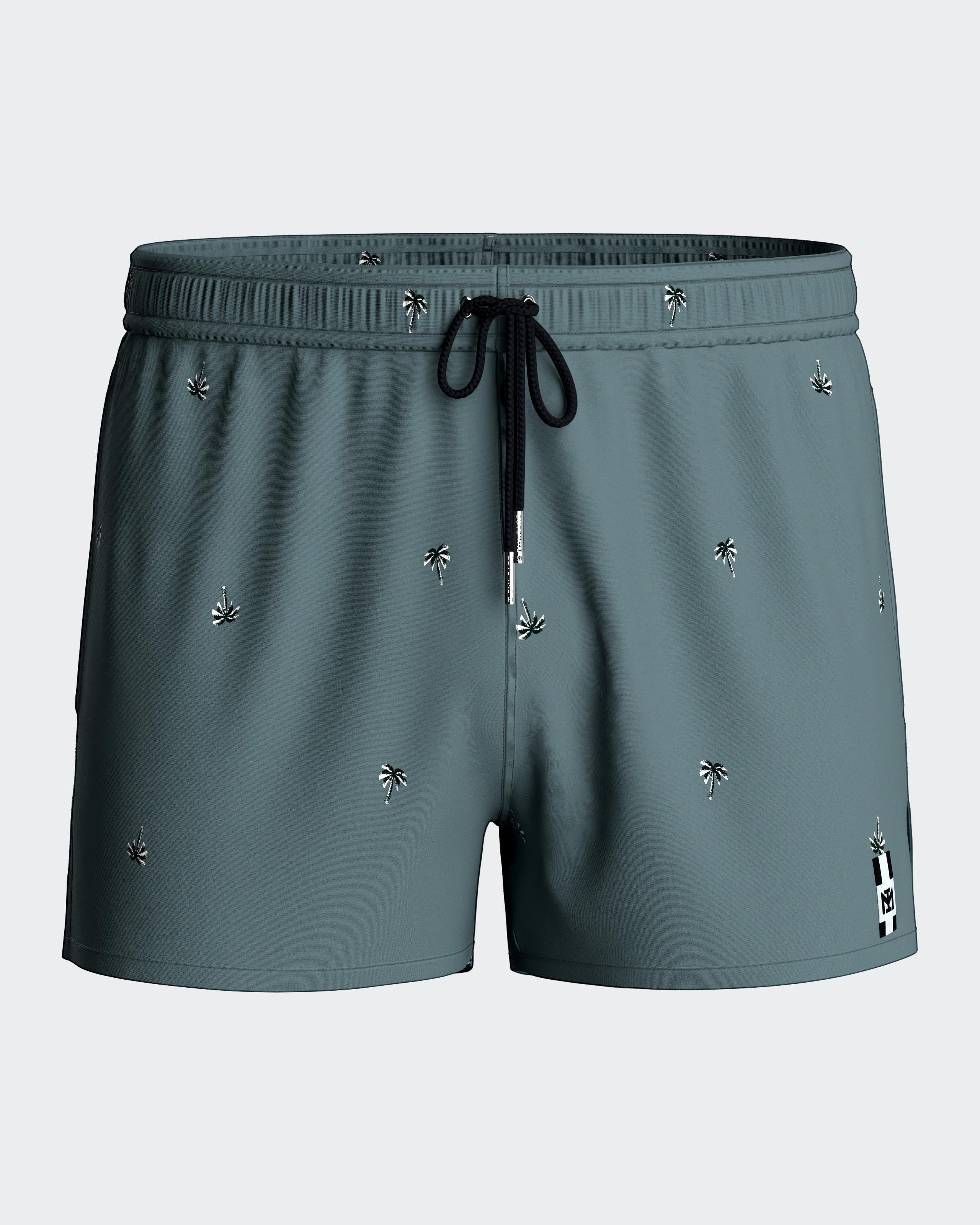 Maison Sarava men's teal swim shorts with tropical micro-motif, elastic waistband, and drawstring.
