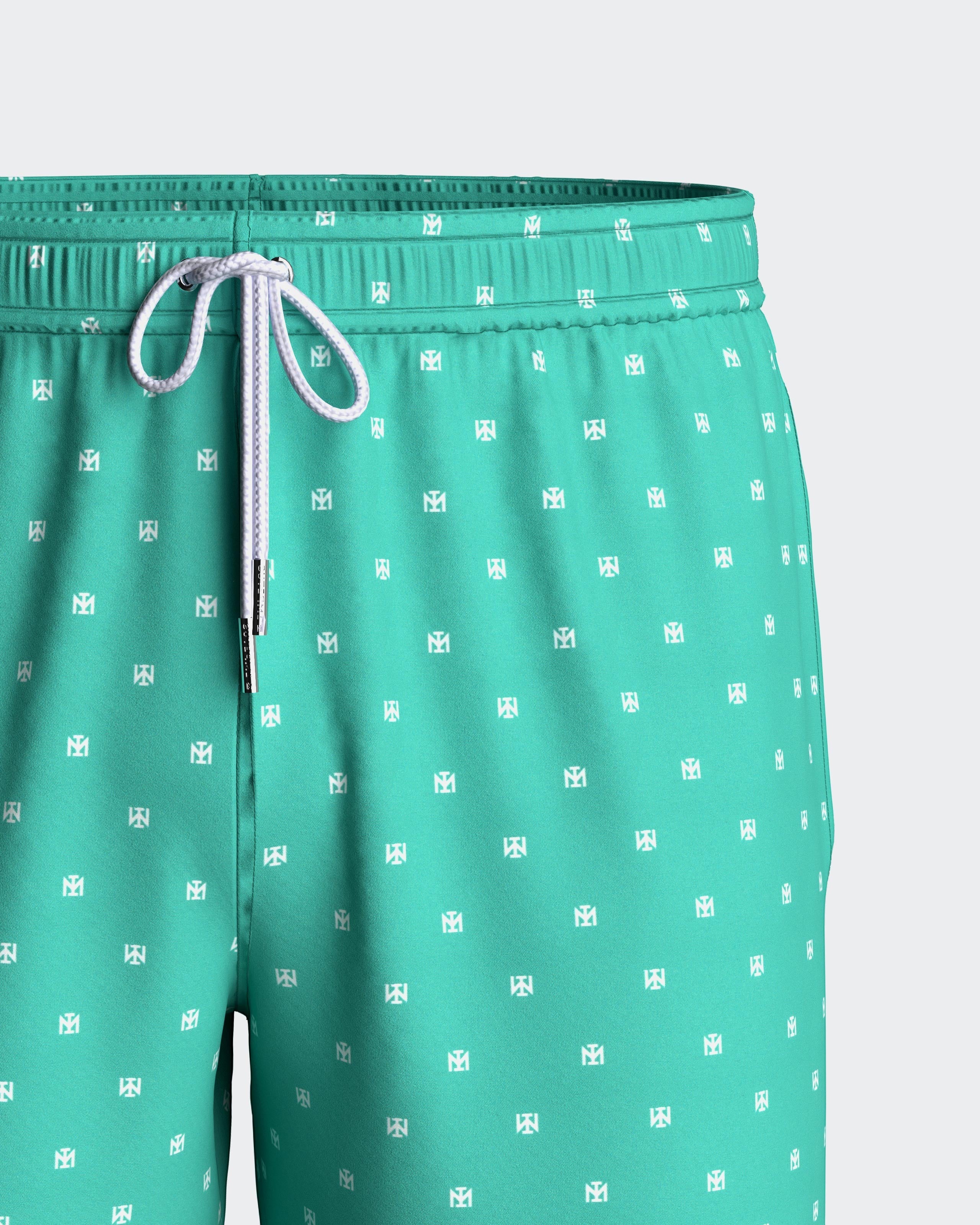 Maison Sarava men's turquoise swim trunks with white micro-pattern logo, drawstring waist, and side pockets.