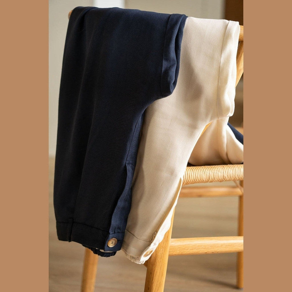 Maison Sarava navy and beige wide leg pleated trousers with button detail, displayed on a wooden chair.