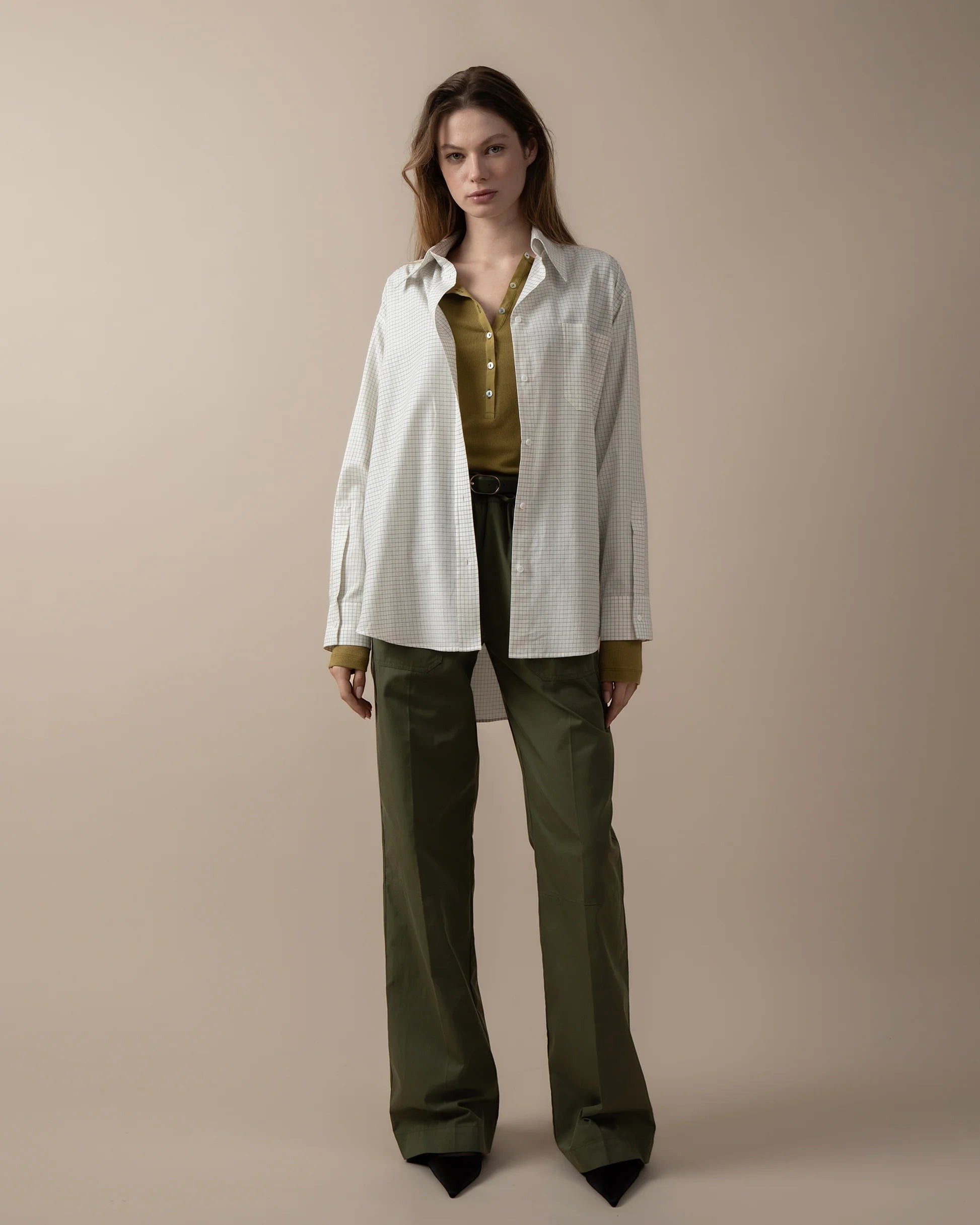Maison Sarava women's oversized white and grey checkered shirt with pointed collar, long sleeves, and round hem, worn over a green top.