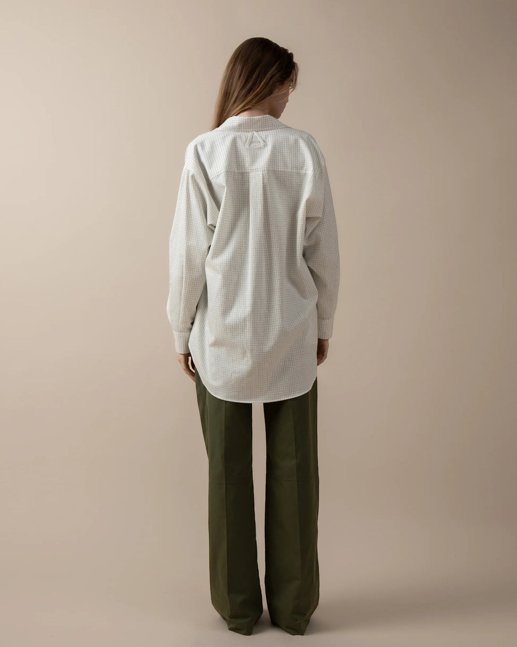 Maison Sarava women's oversized white and blue checkered shirt with pointed collar and button cuffs. Worn with green wide-leg trousers.