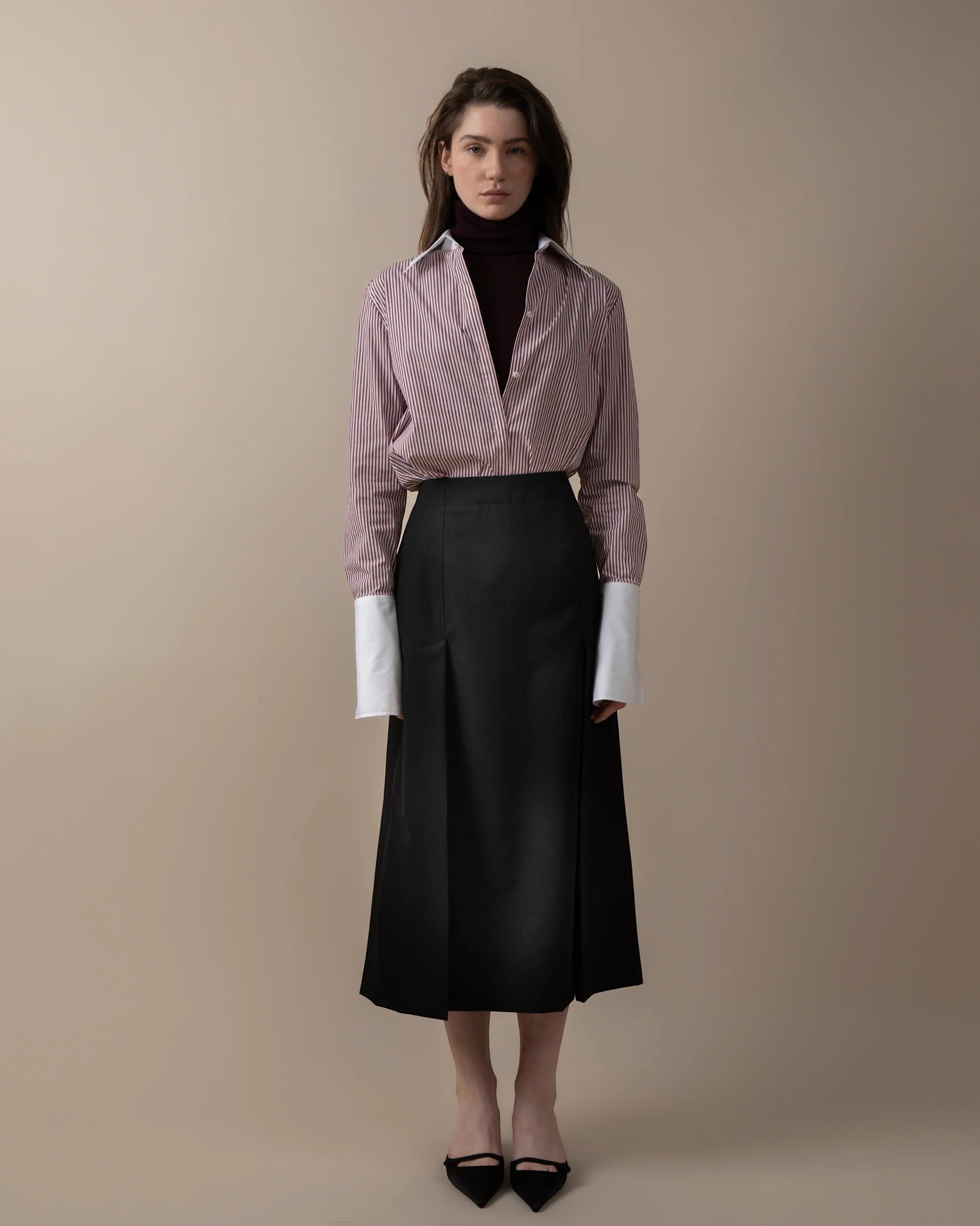 Maison Sarava women's fitted red and white striped shirt with white cuffs, worn over a dark turtleneck and black skirt.
