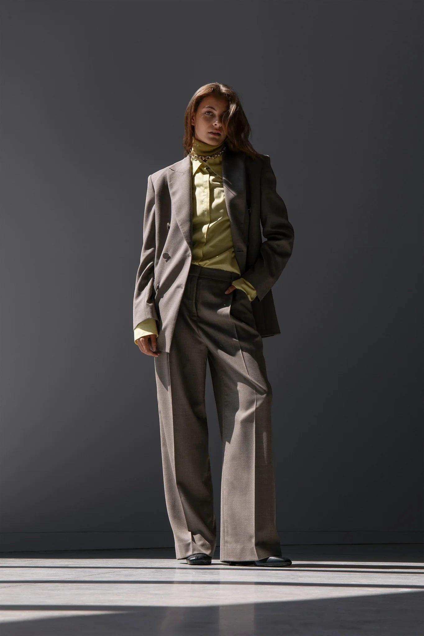 Maison Sarava women's taupe wool double-breasted blazer with peak lapels and flap pockets, paired with matching trousers and a lime green satin shirt.