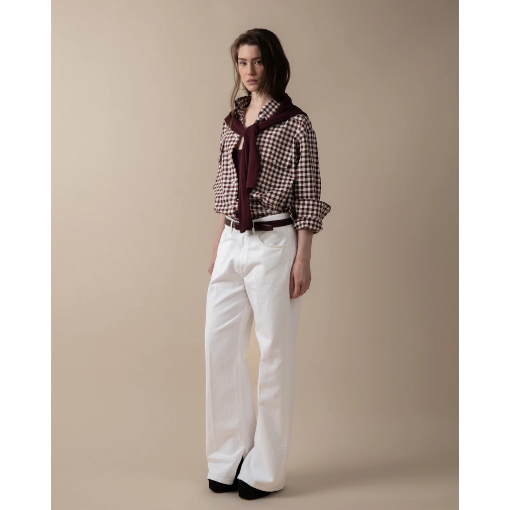 Maison Sarava women's oversized brown and white gingham western shirt with pointed collar, buttoned front, and patch pockets. Model wears white wide-leg pants and a burgundy sweater.