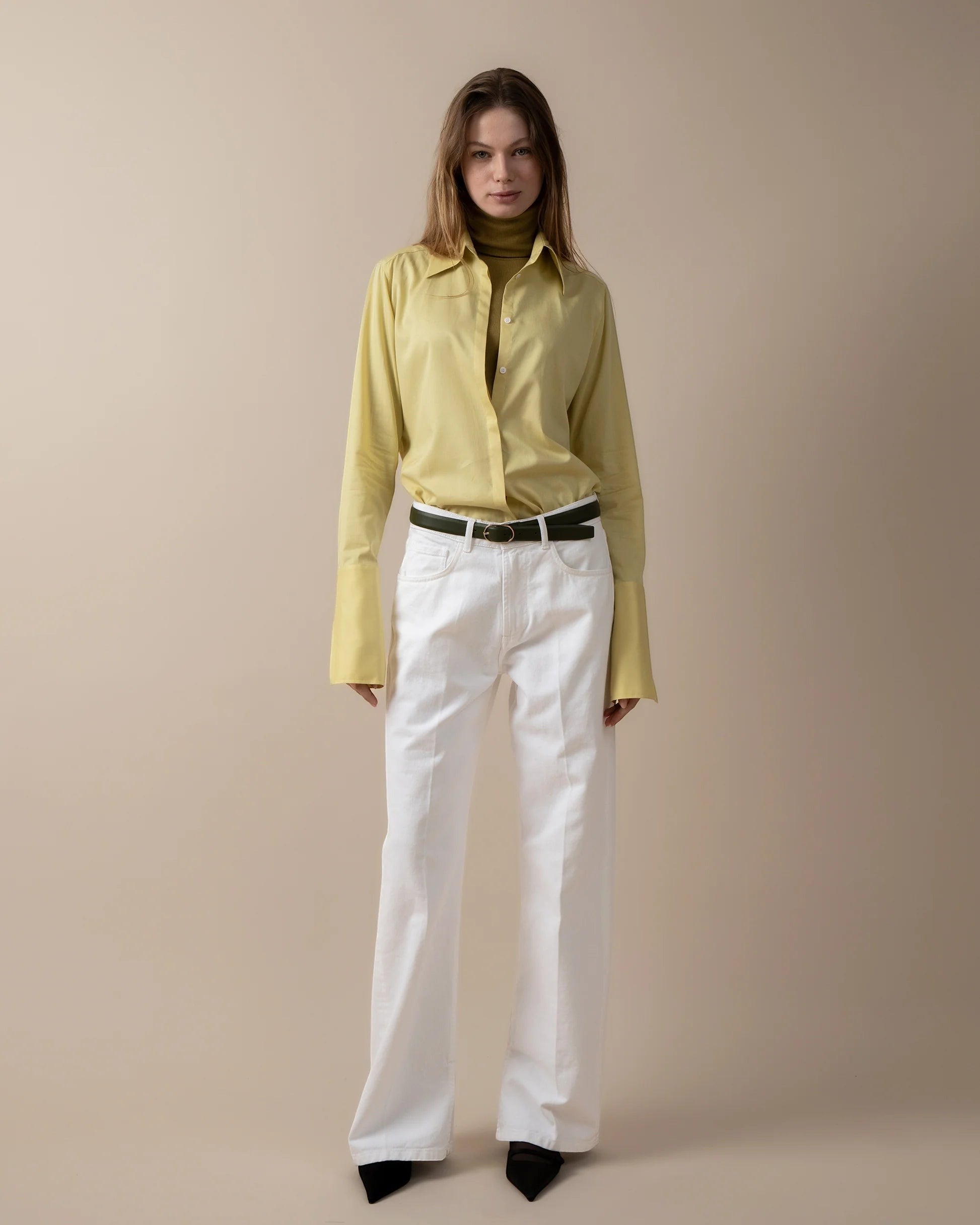Maison Sarava women's fitted yellow long-sleeve shirt with pointed collar and high cuffs, paired with white trousers.